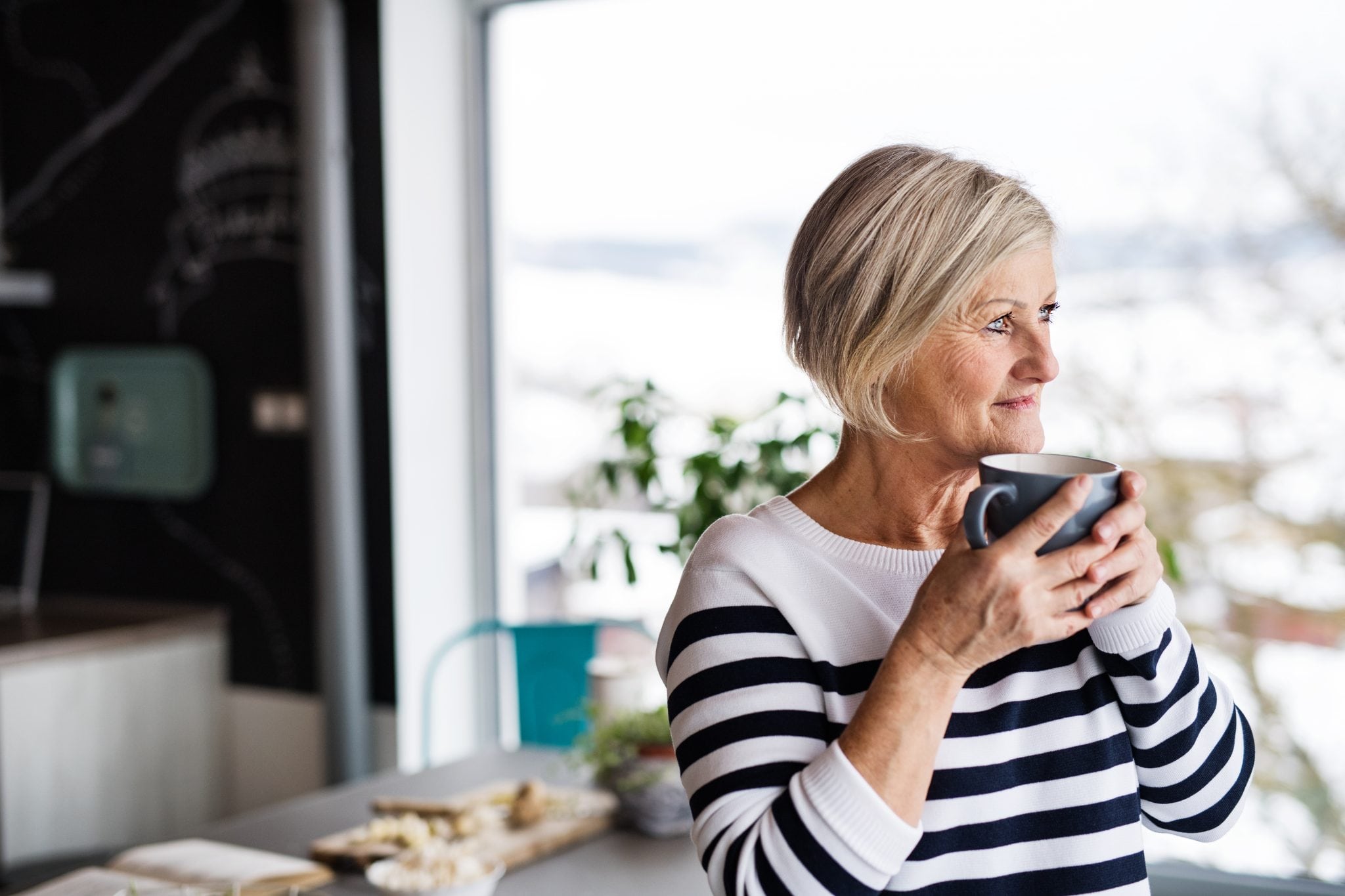 older woman in kitchen drinking coffee wondering why she can hear but not understand